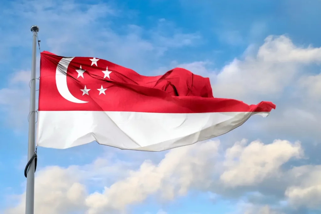 Die Nationalflagge von Singapur weht stolz im Wind vor einem blauen Himmel mit Wolken