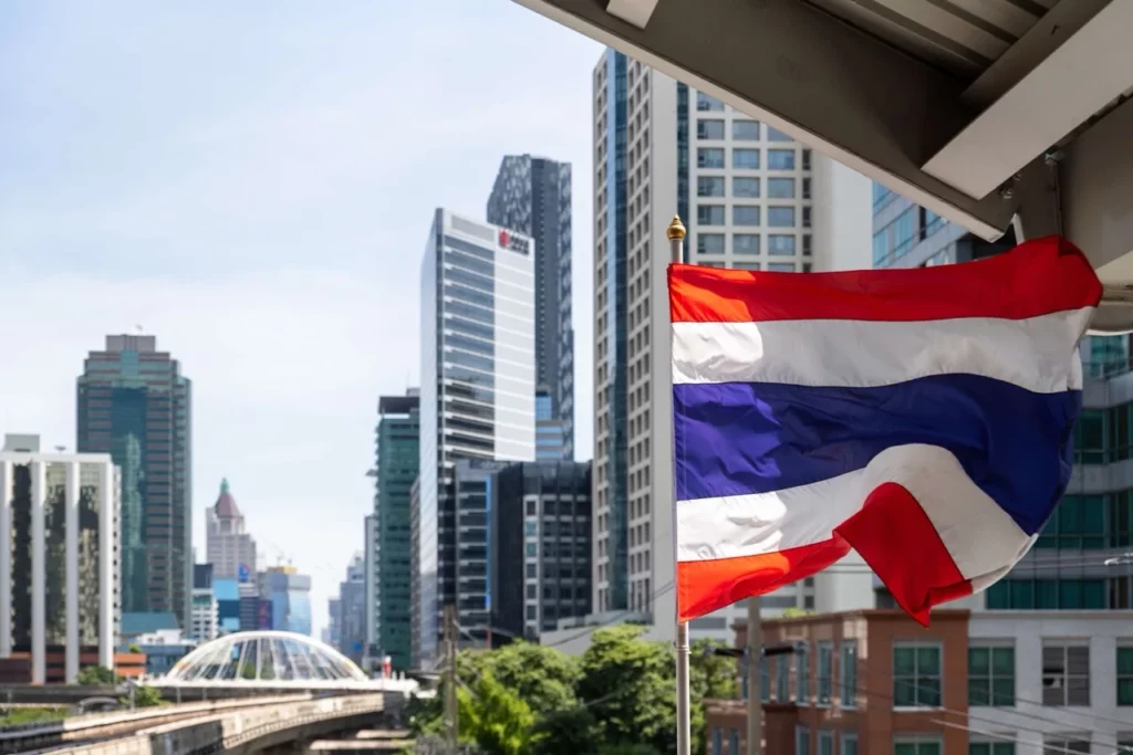 Thailändische Flagge vor der Skyline von Bangkok, die den urbanen Charakter der Stadt und den Stolz des Landes repräsentiert.