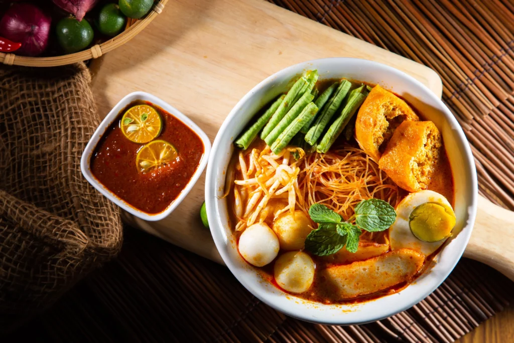 Traditionelle singapurische Laksa-Nudelsuppe mit frischen Beilagen und würziger Sauce