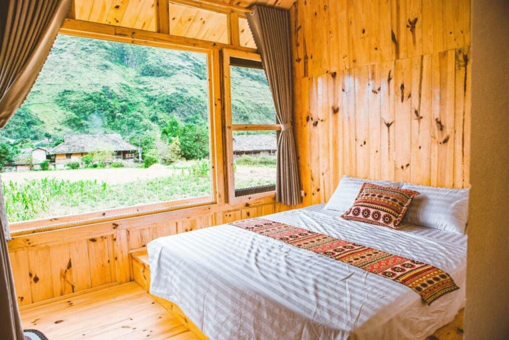 Gemütliches Schlafzimmer aus Holz mit großem Fenster und Blick auf grüne Hügel, perfekt für eine günstige Vietnam Reise.