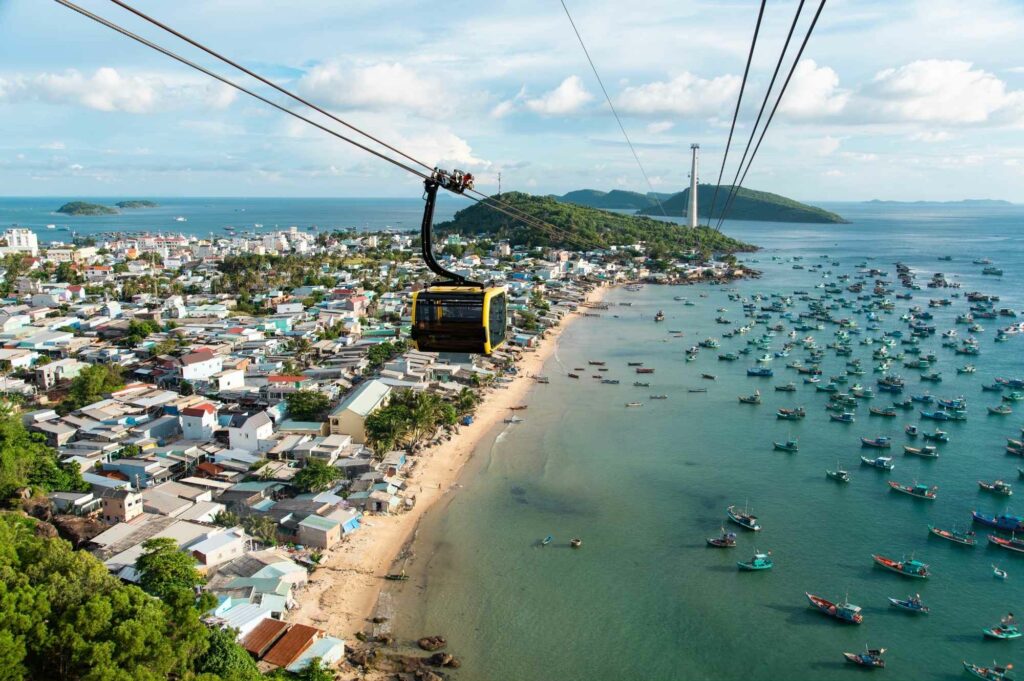 Atemberaubende Luftaufnahme einer Seilbahn, die über die Küste Vietnams gleitet, während Boote auf dem blauen Meer treiben.