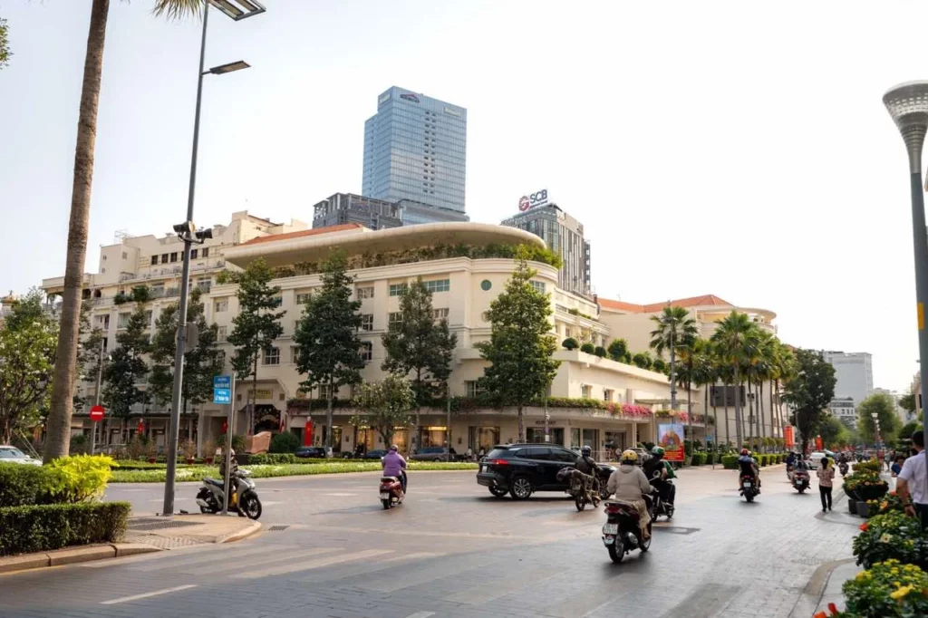 Belebte Stadtstraße in Vietnam, umgeben von modernen Gebäuden und Bäumen unter einem strahlend blauen Himmel.