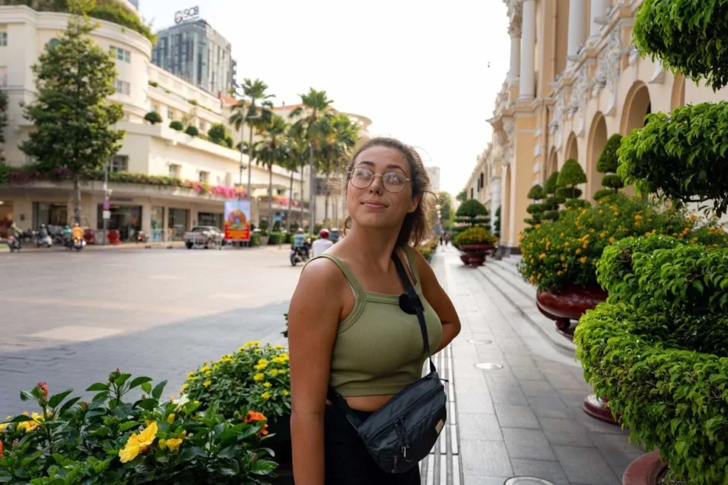 Clara steht inmitten lebhafter vietnamesischer Straßen, üppiger Pflanzen und farbenfroher Gebäude im Kolonialstil.
