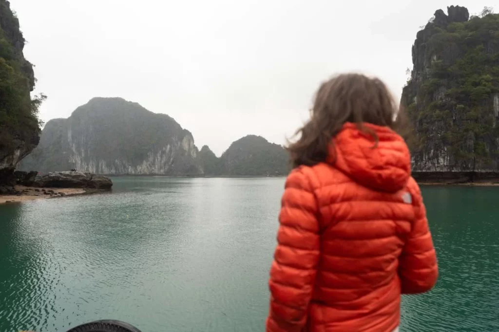 Clara in einer orangefarbenen Jacke genießt Vietnams ruhige Bucht mit majestätischen Felsklippen in der Ha Long Bay.