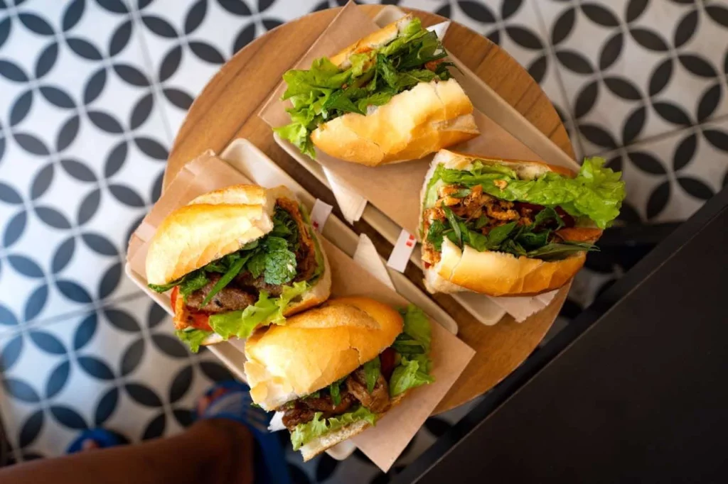 Frische Banh-Mi-Sandwiches mit Gemüse auf einem Holztisch, der das klassische Vietnam-Flair widerspiegelt.