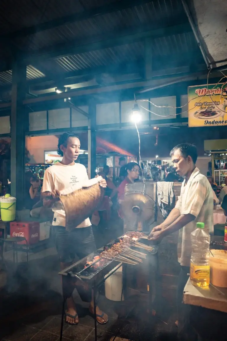 Der Nachtmarkt von Sanur mit einem Local der typische Satay Spieße, balinesisches Streetfood, auf einem Grill zubereitet.