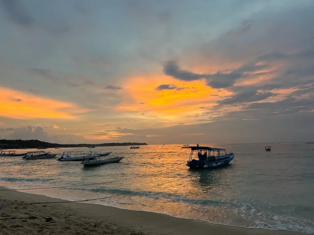 Der leuchtend orange Sonnenuntergang spiegelt sich im ruhigen Meer wider als Highlight beim Bali Backpacking.