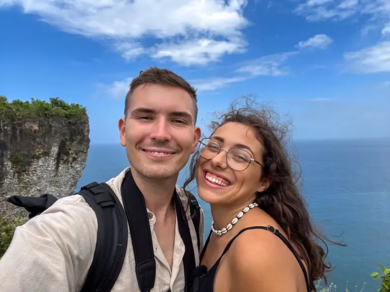 Clara und Jonathan machen ein Selfie auf Balis Klippe mit atemberaubendem Meerblick und klarem blauen Himmel.