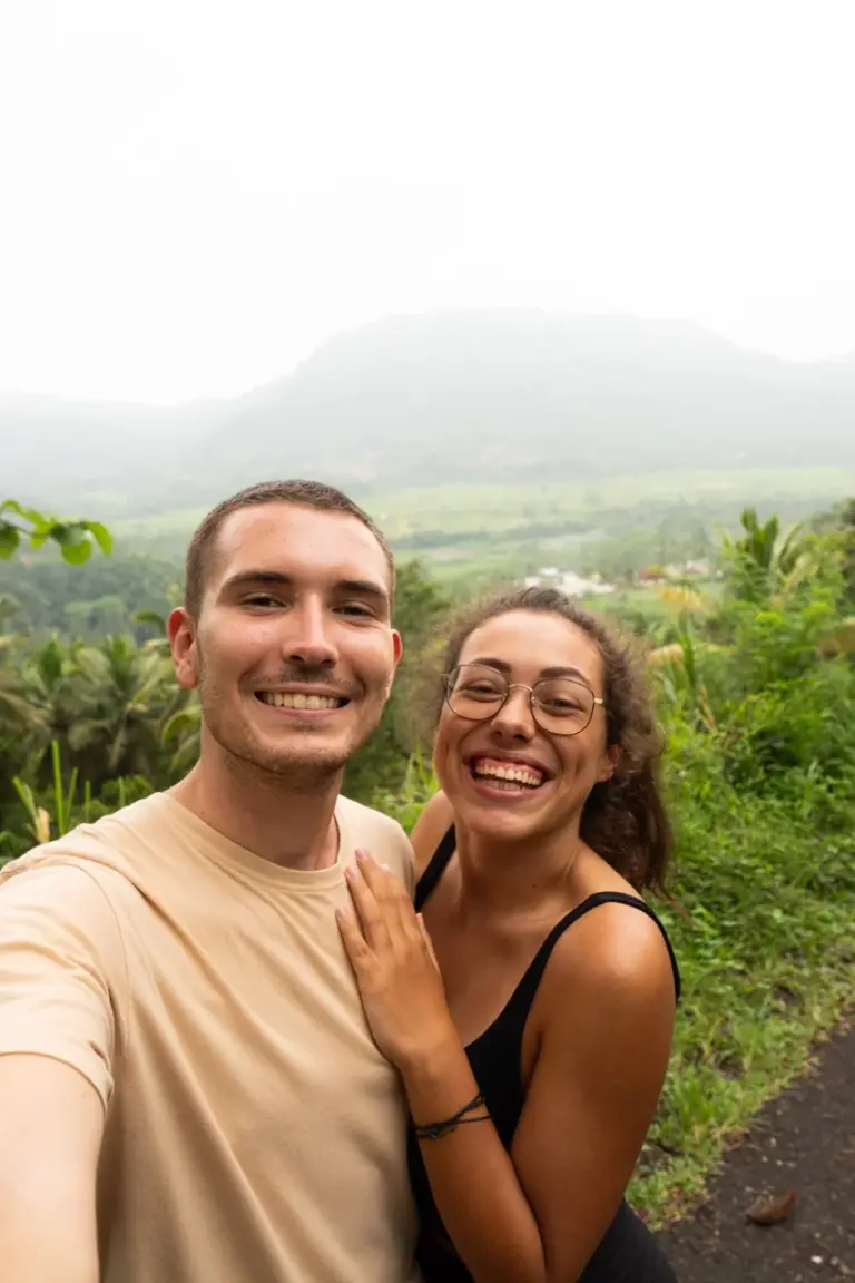 Clara und Jonathan machen ein Selfie inmitten der üppig grünen Hügel Balis  mit Reisfeldern und Bergen im Hintergrund auf der Weltreise.