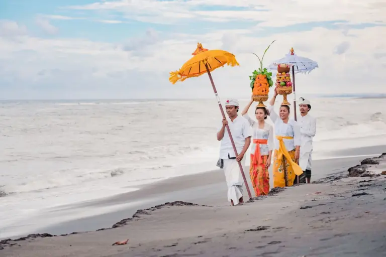 Eine typische Zeremonie auf Bali mit mehreren Menschen am Strand in traditioneller Kleidung und besonderer Ausstrahlung.
