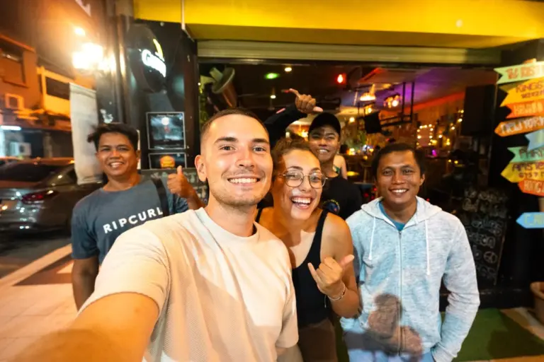 Fünf Freunde lachen unter Neonlichtern, während sie nachts mit dem Rucksack durch das pulsierende Kuala Lumpur reisen.