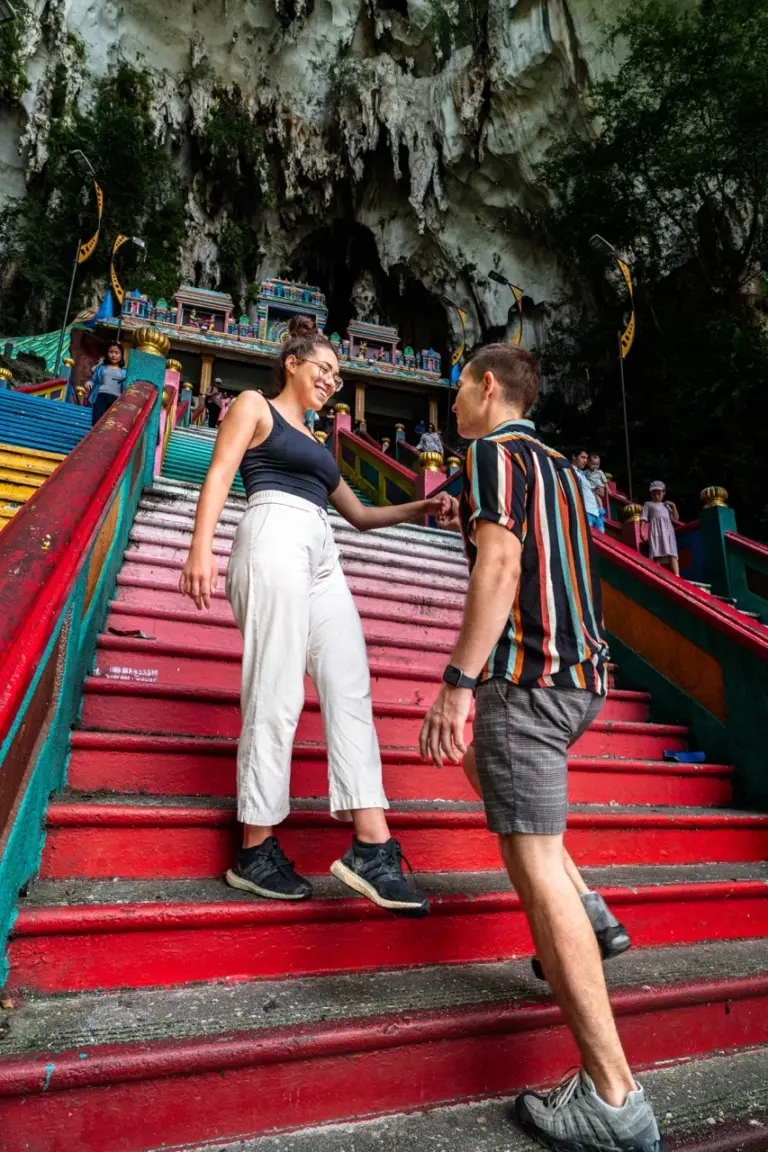 Clara und Jonathan auf einer bunten Treppe neben einem Höhleneingang in Malaysia an den Batu Caves.