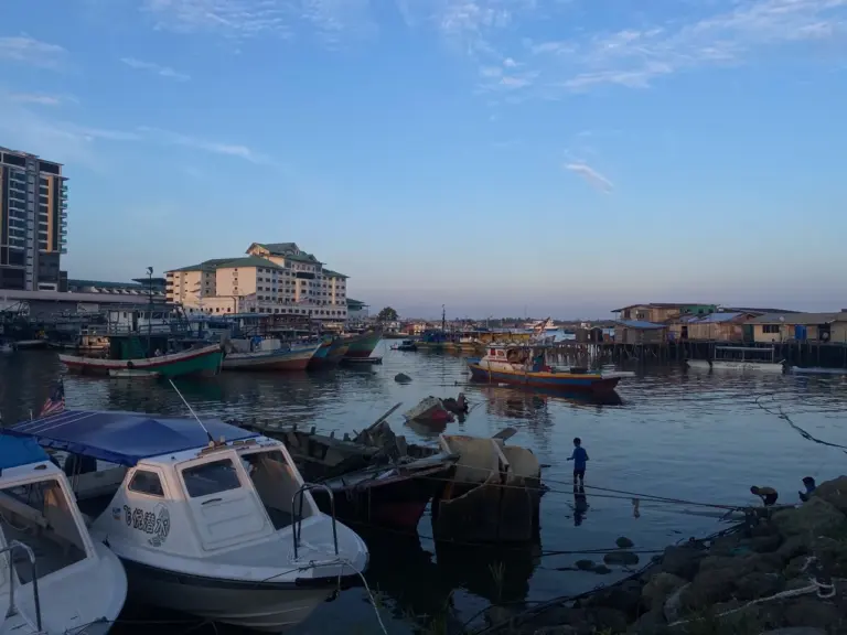 Boote liegen im Hafen von Malaysia Borneo, eingerahmt von Gebäuden und einem klaren blauen Himmel.