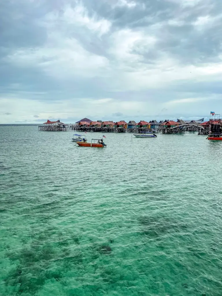 Wasser Bungalows über türkisfarbenem Meer auf der Insel Mabul in Malaysia (Borneo) unter einem bewölkten Himmel.