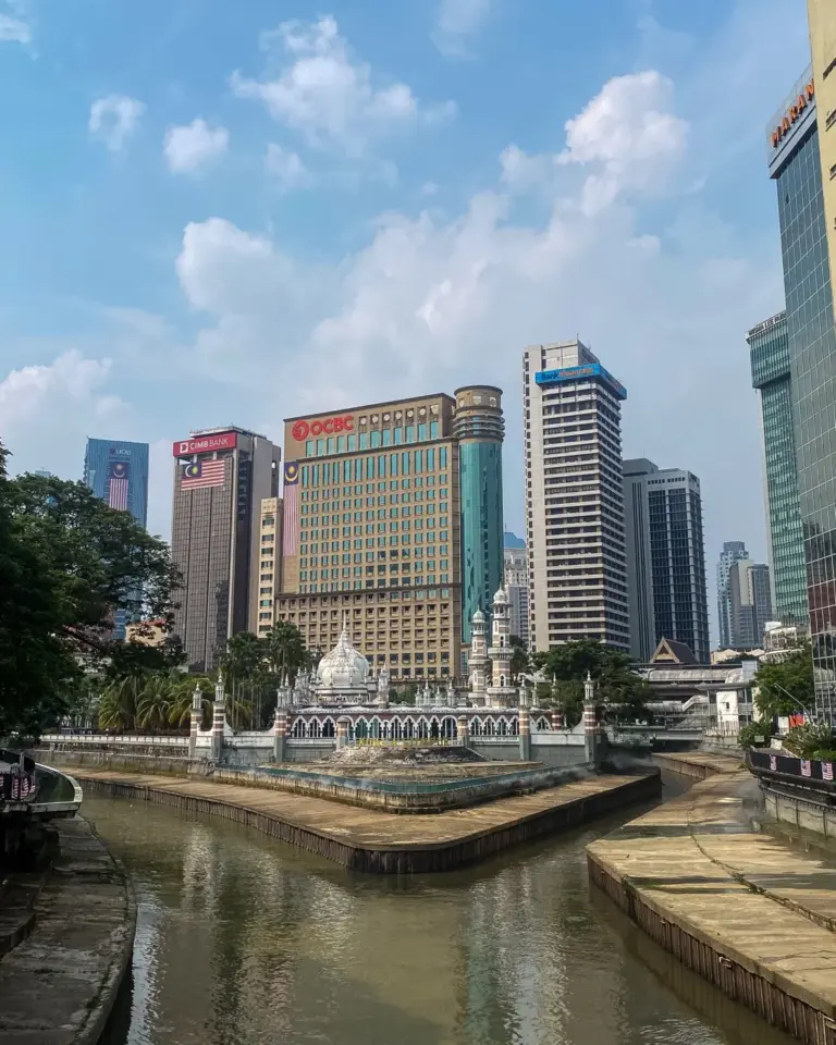 Die Skyline Malaysias ist geprägt von einer Moschee am Flussufer, im Hintergrund Wolkenkratzer.