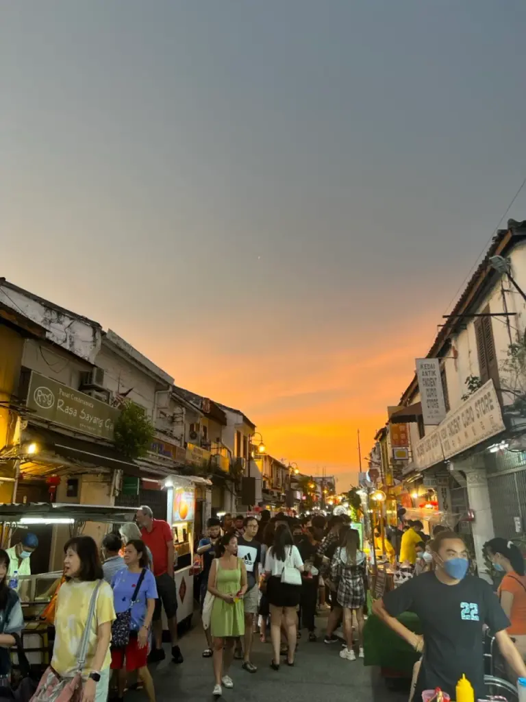 Sonnenuntergang auf einem lebhaften malaysischen Nachtmarkt, umrahmt von leuchtend orangefarbenem Himmel zur besten Malaysia Reisezeit.