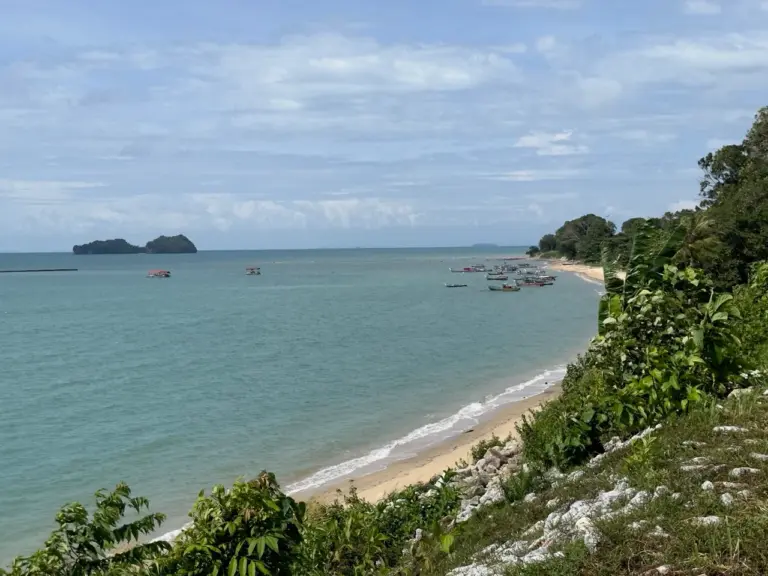 Clara entspannt an einem malaysischen Sandstrand, umgeben von üppigem Grün und mit Blick auf ferne Inseln.