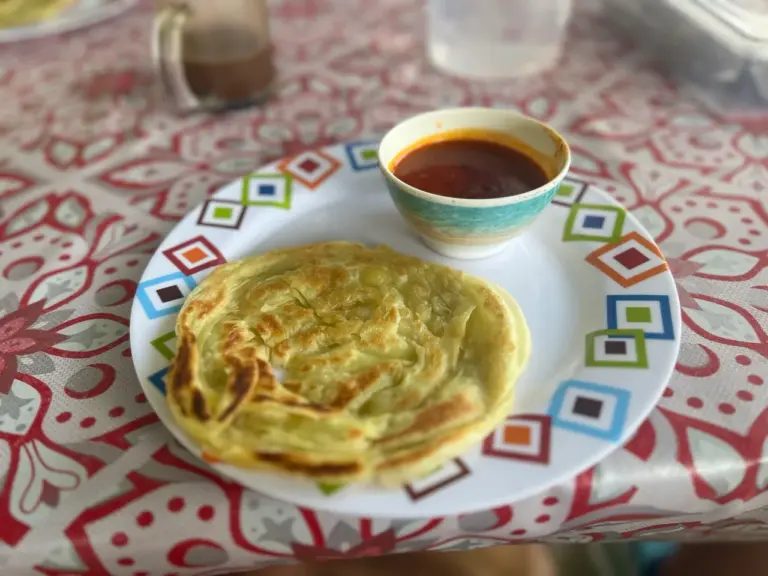 Roti Canai und Curry liegen auf einer farbenfrohen Tischdecke und verlocken den Rucksacktouristen Malaysias zum Verweilen.