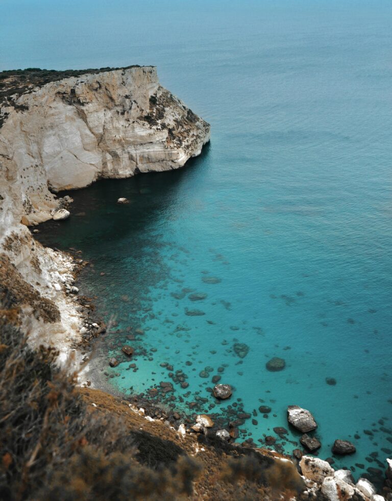 Türkisfarbenes Meer trifft unter klarem Himmel auf felsige Klippen, perfekt als Inspiration für den Urlaub 2025.