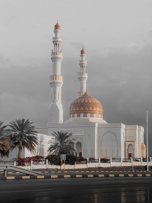 Eine große Moschee mit zwei Minaretten und einer Kuppel ragt inmitten von Palmen unter einem wolkigen Himmel empor, perfekt für Reiseziele 2025.