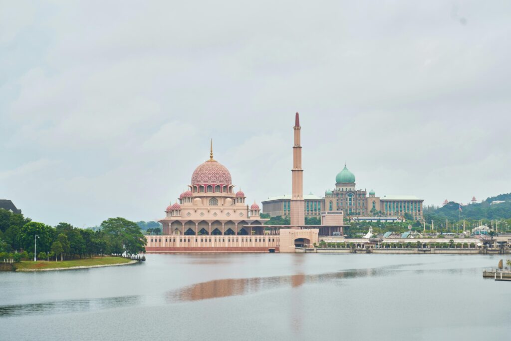 Die schöne Putra-Moschee mit der rosa Kuppel an einem ruhigen See unter bewölktem Himmel in Malaysia.