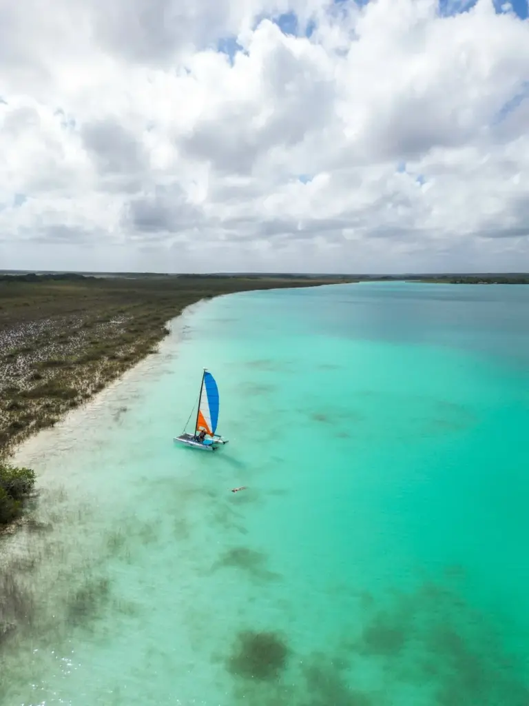 Segelboot gleitet mit blauen und orangefarbenen Segeln über das türkisfarbene Meer, ideal für den Sommerurlaub mit Abenteuern im Jahr 2025.