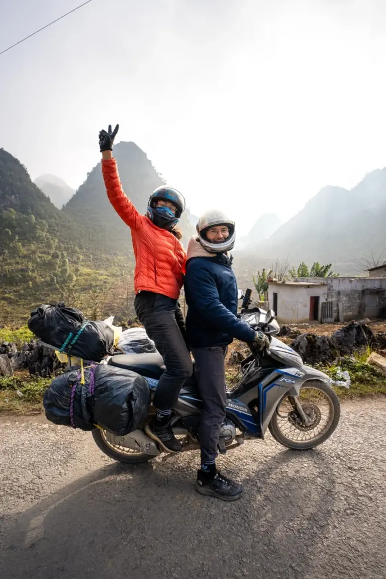 Clara und Jonathan mit all ihrem Weltreise Gepäck auf einem beladenen Motorrad vor den Bergen Vietnams.