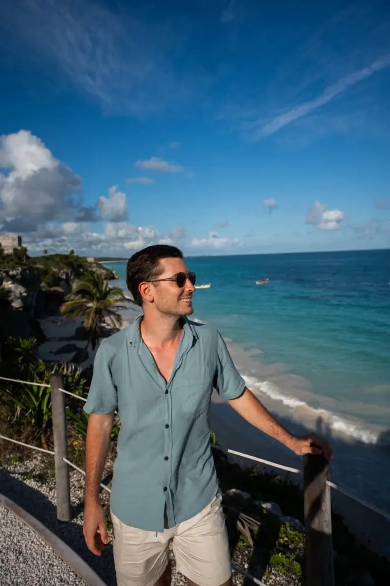 Jonathan an einer Klippe mit Palmen unter einem strahlend blauen Himmel als Inspiration für Weltreise Kleidung.