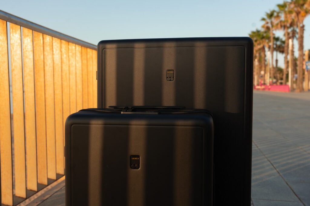 Zwei schwarze Koffer auf einer sonnigen, von Palmen gesäumten Strandpromenade, gerade im Hartschalenkoffer Test.