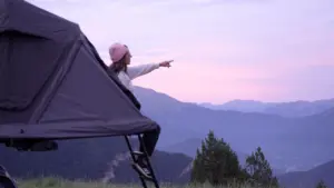 Clara auf der Roof Space 2 Dachzelt Leiter mit rosafarbenen Wolken bei Sonnenuntergang und Blick auf die Berge in der Ferne.