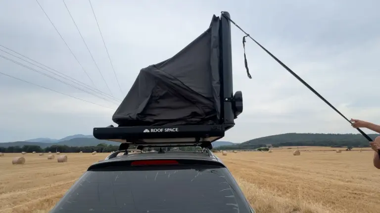 Ein Roof Space 2 Dachzelt auf einem Auto in einem goldenen Erntefeld, Jonathan zieht den Entfaltungsgurt.