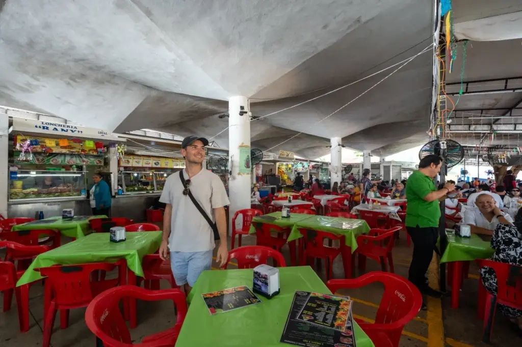 Jonathan in einem lebhaften Yucatan-Markt mit roten Stühlen und grünen Tischdecken im Mercado Lucas de Gálvez.