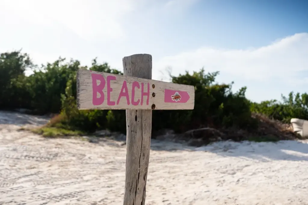 Das hölzerne BEACH-Schild mit einer Muschel zeigt direkt auf die Küste von Yucatan, ideal für tropische Reisestimmung.