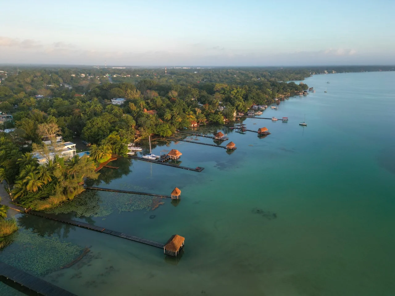 Luftaufnahme eines ruhigen Yucatan-Sees mit hölzernen Anlegestellen und gemütlichen Hütten am Seeufer, Mexiko-Reiselandschaft.