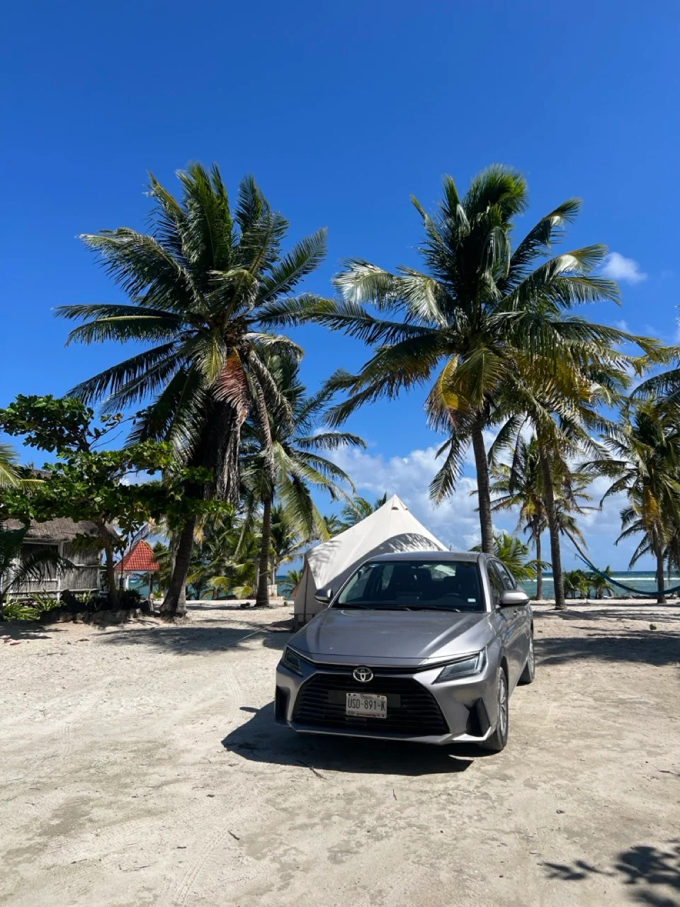 Ein silberner Mexiko Mietwagen steht am Sandstrand von Yucatan bei strahlend blauem Himmel im sonnigen Mexiko.