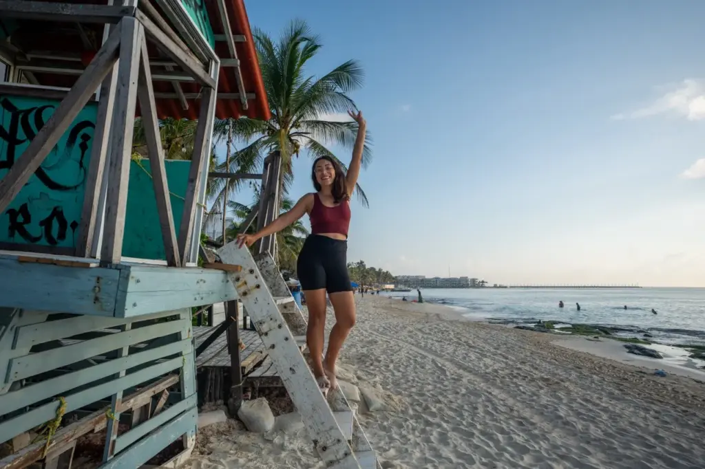 Clara sitzt auf einer hölzernen Rettungsschwimmerleiter an einem Sandstrand in Yucatan mit Palmen und blauem Himmel, wunderschöne Yucatan Sehenswürdigkeiten.