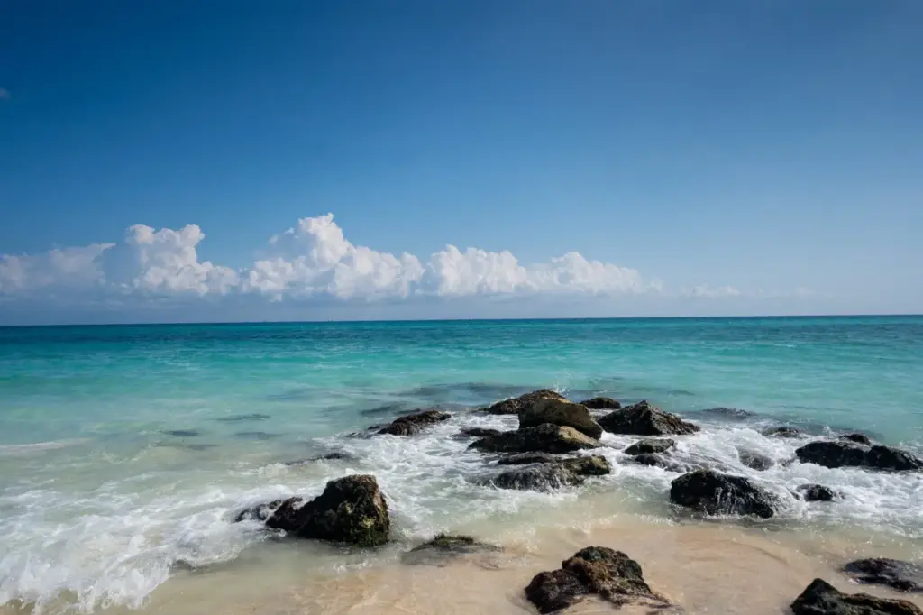 Ein Strand als eine von vielen Yucatan Sehenswürdigkeiten, mit seinem sandigen Ufer, den Felsen, dem klaren blauen Himmel und den weit entfernten Wolken bietet eine friedliche Kulisse.
