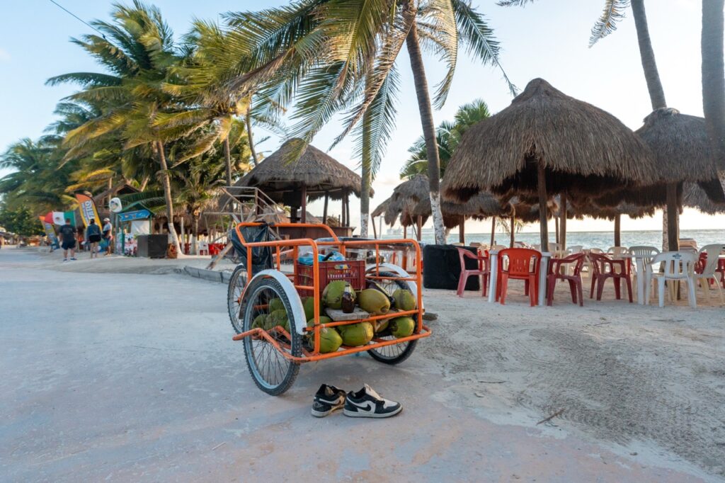 Ein Fahrrad mit Kokosnüssen und Schuhen an einer sonnigen Strandstraße an der Küste von Yucatan.