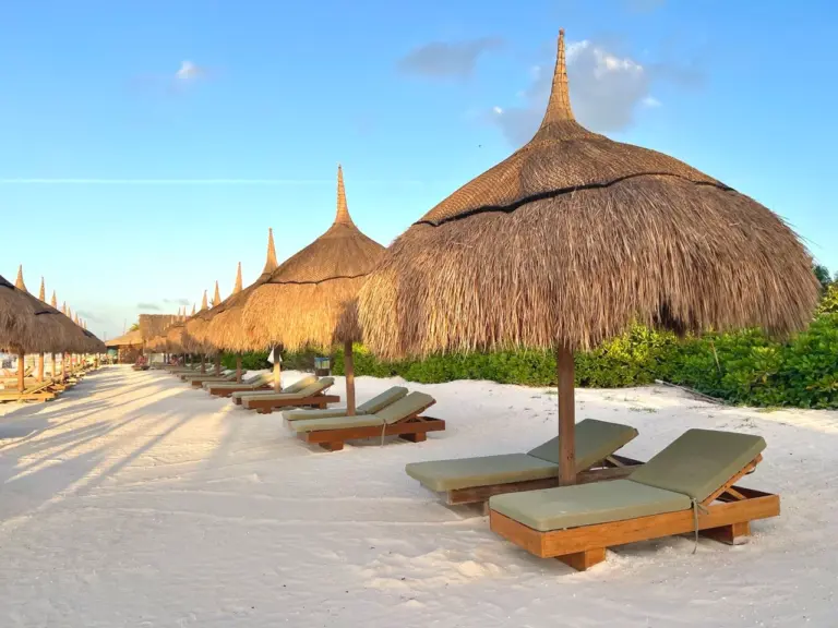 Hölzerne Liegen und strohgedeckte Sonnenschirme säumen den Sandstrand von Yucatan Beach in Mexiko.