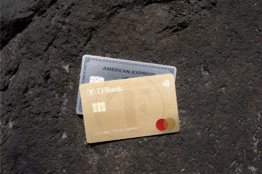 Goldene TF Bank- und graue American Express-Karten ruhen auf dunklem Stein, perfekt für Reiseabenteuer weltweit.