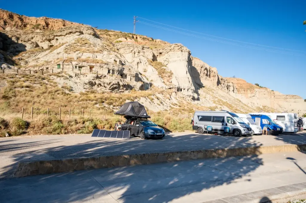Autos, Wohnmobile und ein Dachzelt mit Sonnenkollektoren an felsigen Klippen unter einem strahlend blauen Himmel.