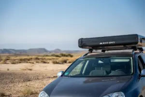 Ein Auto mit Dachzelt steht in einer sonnigen, trockenen Landschaft mit Hügeln in der Ferne.