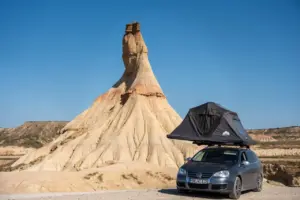Ein Auto mit Dachzelt, geparkt zwischen markanten Wüstenfelsen unter strahlend blauem Himmel, perfekt für Abenteuer.