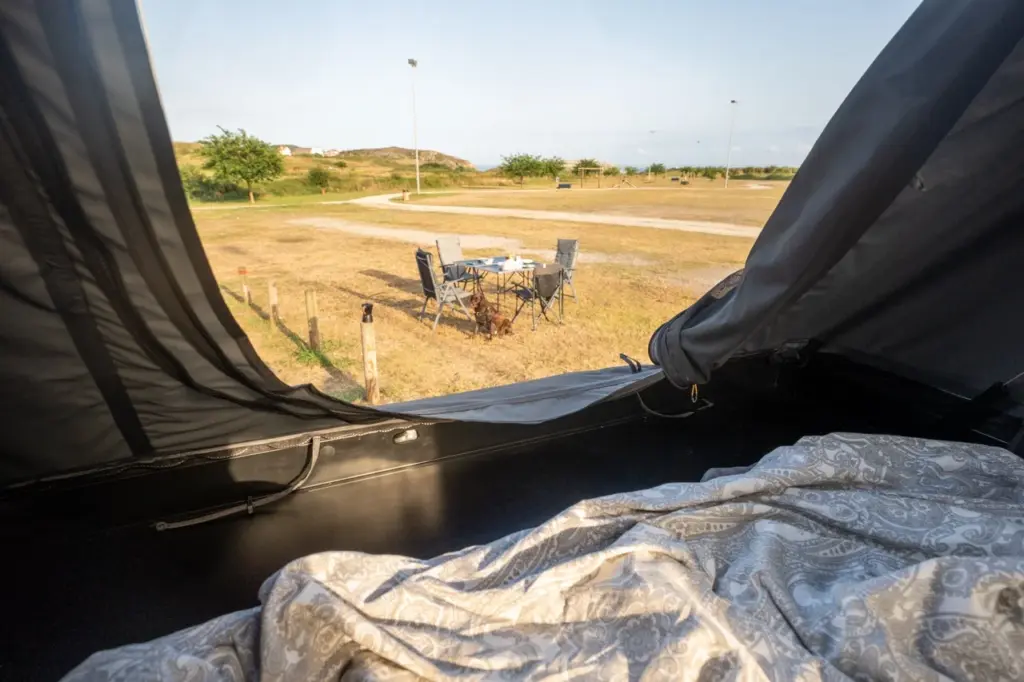 Gemütliches Dachzelt-Interieur mit einem bequemen Bett mit Blick auf einen Tisch und Stühle im Freien auf grünem Gras.