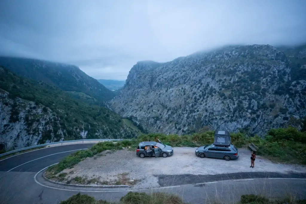 Zwei Autos mit Dachzelt auf einem nebelverhangenen Berg geparkt, Clara genießt die Aussicht in der Ferne.