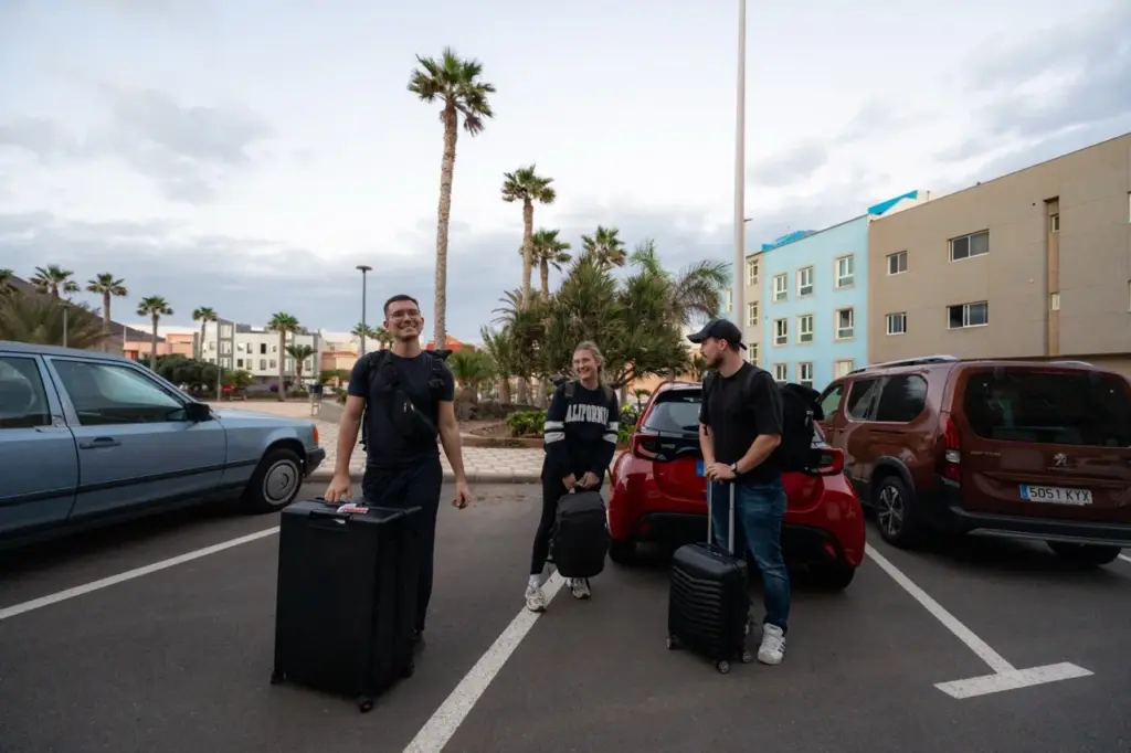 Clara und Jonathan mit einem Freund, plus Gepäck, auf einem Grundstück auf Gran Canaria zwischen Palmen und dem Hotel Bohemia Suites.