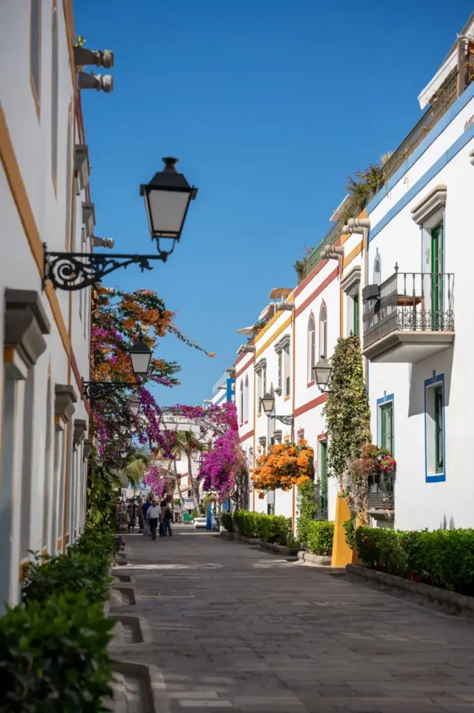 Charmante Straße auf Gran Canaria mit weißen Gebäuden, Blumen, Balkonen und Laternen unter blauem Himmel.