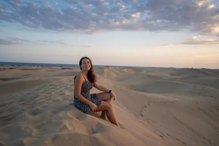 Clara genießt die goldenen Dünen Gran Canarias bei Sonnenuntergang mit einem strahlenden Lächeln unter einem teilweise bewölkten Himmel.