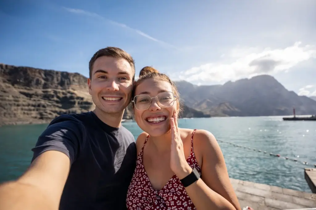 Clara und Jonathan an einem glitzernden See mit den Bergen Gran Canarias und dem blauen Himmel im Hintergrund.