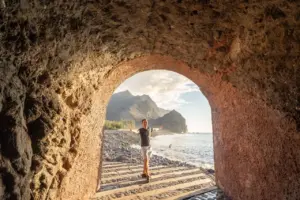 Jonathan am felsigen Tunneleingang an der Küste Gran Canarias, mit den Bergen im Hintergrund.